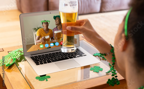 African american woman holding a beer glass having a video call on laptop at home