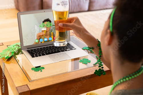 African american woman holding a beer glass having a video call on laptop at home