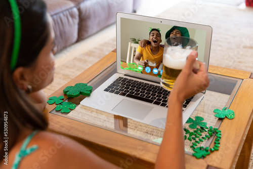 Caucasian woman holding beer having st patrick's day video call with males friend on laptop at home