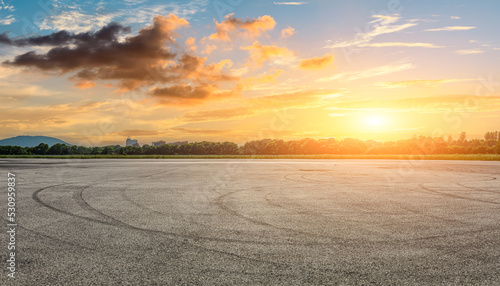 Empty asphalt race track road and green forest with sky clouds at sunset