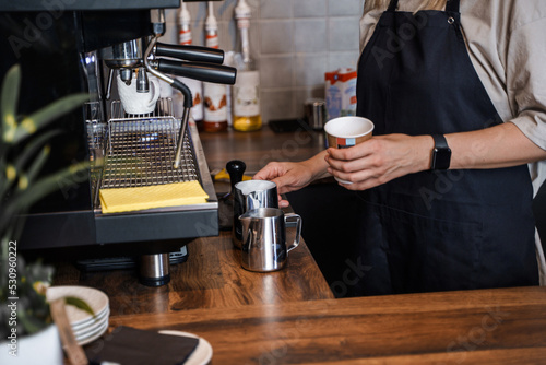 Shot of woman barman with apron preparing milk for coffee in coffee shop.