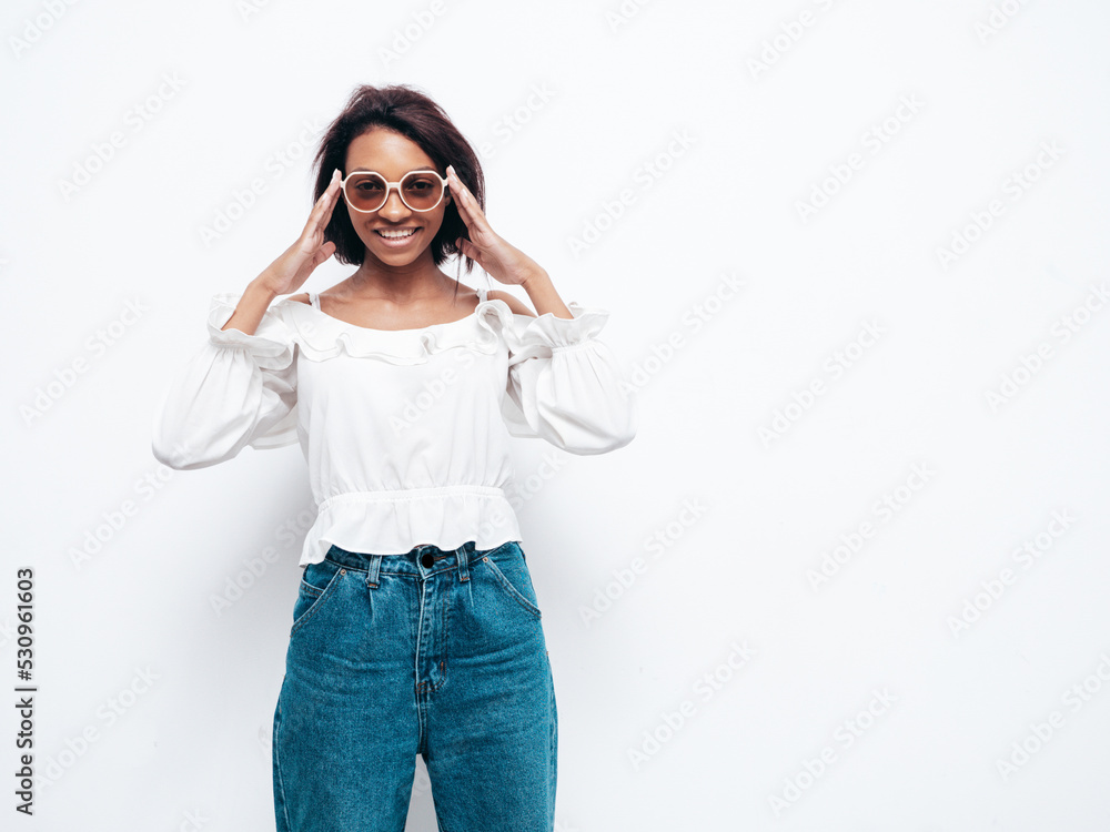 Portrait of young beautiful black woman. Smiling model dressed in summer jeans clothes. carefree female posing near white wall in studio. Tanned and cheerful Portrait of young beautiful black woman. Smiling model dressed in summer jeans clothes. carefree female posing near white wall in studio. Tanned and cheerful