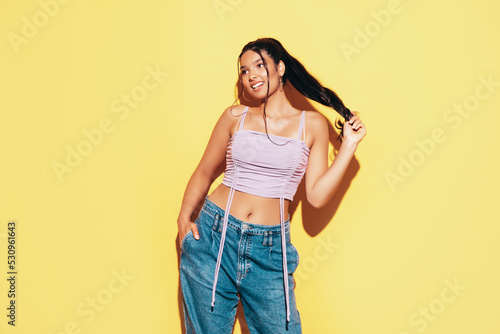 Young beautiful smiling female in trendy summer jeans and top clothes. Carefree woman posing near yellow wall in studio. Sexy positive model having fun indoors. Cheerful and happy