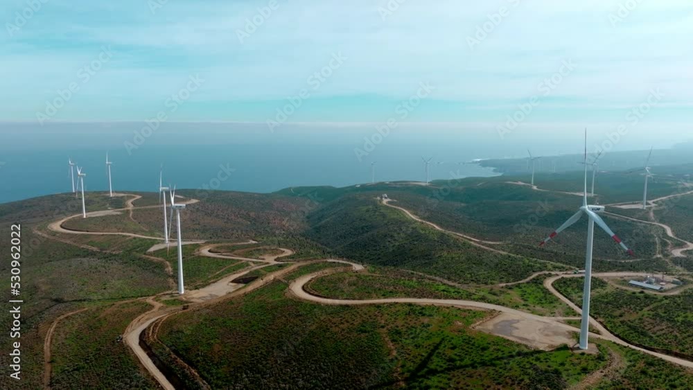Drone flying towards windmills spinning on forested hilltop, wind farm in northern Chile oceanfront Drone flying towards windmills spinning on forested hilltop, wind farm in northern Chile oceanfront
