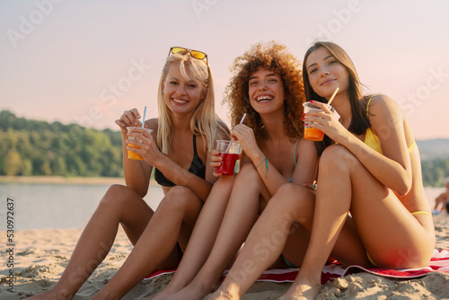 Three young women drinking juice on the beach, having fun  © Tijana