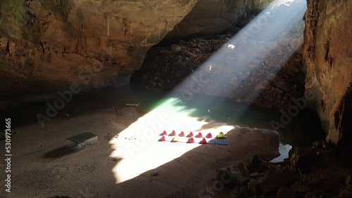 Drone backward shoot of sunbeam down to tents in a big cave  photo