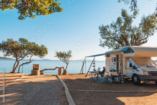 Family traveling with motorhome are eating breakfast on a beach. Travelers on an active family vacation with motorhome RV parked on the beach under a tree facing the sea, Crete, Greece.