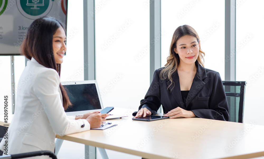 Closeup shot of Millennial Asian beautiful successful professional female businesswoman employee in formal suit sitting smiling talking to colleagues at working desk in company office meeting room Closeup shot of Millennial Asian beautiful successful professional female businesswoman employee in formal suit sitting smiling talking to colleagues at working desk in company office meeting room