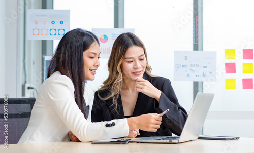 Millennial Asian successful professional female businesswomen in formal suit sitting discussing helping solving problem working with laptop notebook computer together in company office meeting room