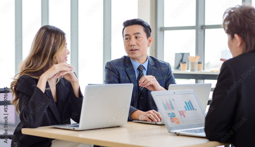 Millennial Asian successful professional male businessman female businesswoman in formal suit sitting together at working desk with laptop computer talking sharing business ideas in company office