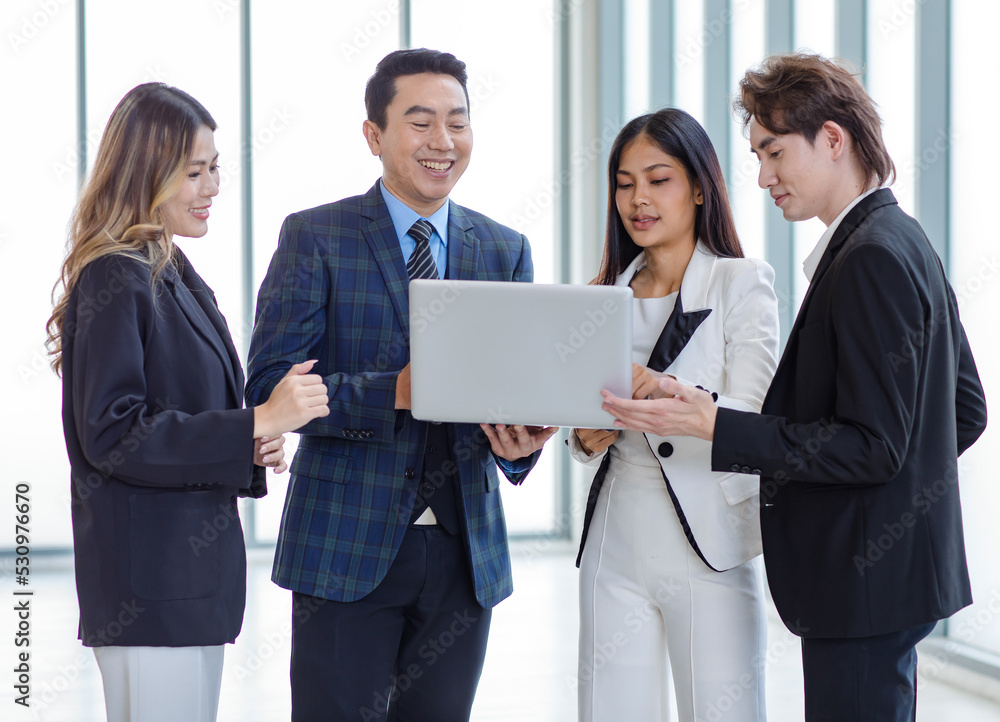 Millennial Asian successful professional businessman manager mentor in formal suit standing holding laptop computer talking helping advising male and female businesswomen colleagues in company office Millennial Asian successful professional businessman manager mentor in formal suit standing holding laptop computer talking helping advising male and female businesswomen colleagues in company office