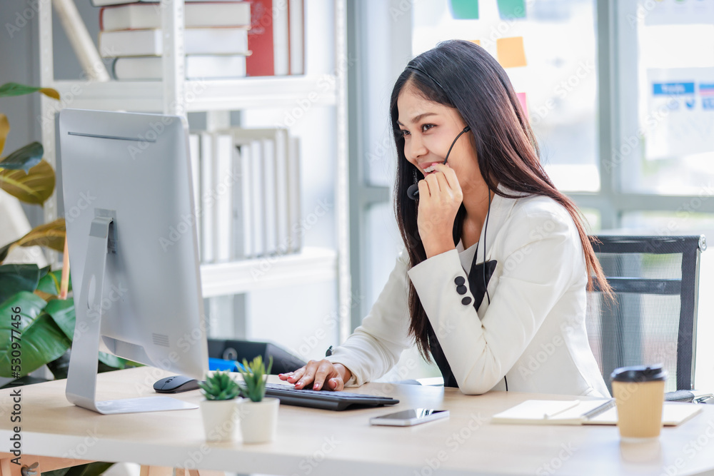Millennial Asian successful professional female businesswoman secretary in white formal suit sitting smiling using smartphone talking negotiating with customer at working desk in company office room Millennial Asian successful professional female businesswoman secretary in white formal suit sitting smiling using smartphone talking negotiating with customer at working desk in company office room