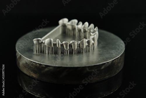 Close-up studio shot on milled metal frame for dental implants on the black background. Concept of new technologies in dental prosthetics