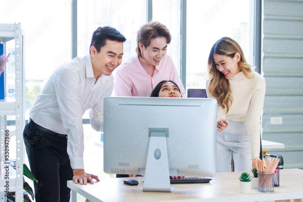 Millennial Asian beautiful successful professional businesswoman sitting smiling pointing finger showing data information on computer monitor to male businessmen female colleague in company office