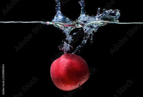Red apple floating in water with splashes on black