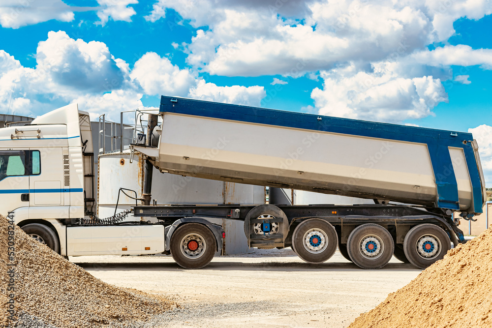 Large dump truck near the concrete factory. Car tonar for transportation of heavy bulk cargo. Provision of crushed stone and gravel for concrete production.
