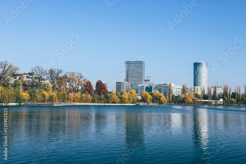 View of yellow autumn trees on the lake with reflection and modern buildings behind