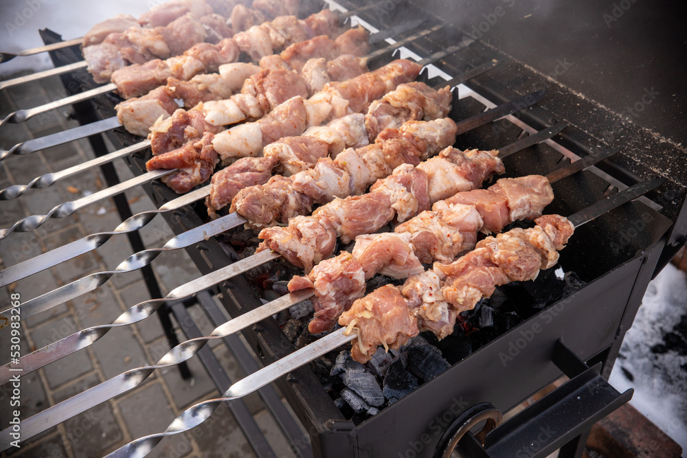 Pieces of raw meat are fried on metal skewers over coals.