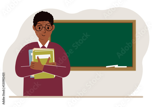 Male teacher with books on the background of the school board.