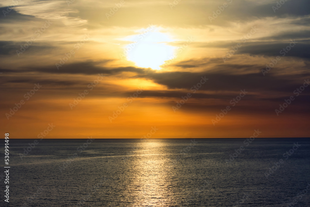 Stunning warm sunset in a dramatic sky above a serene, calm ocean
