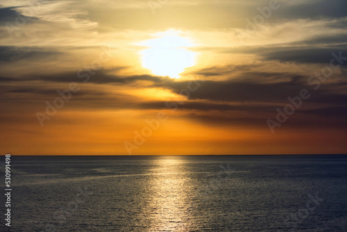 Fototapeta Naklejka Na Ścianę i Meble -  Stunning warm sunset in a dramatic sky above a serene, calm ocean