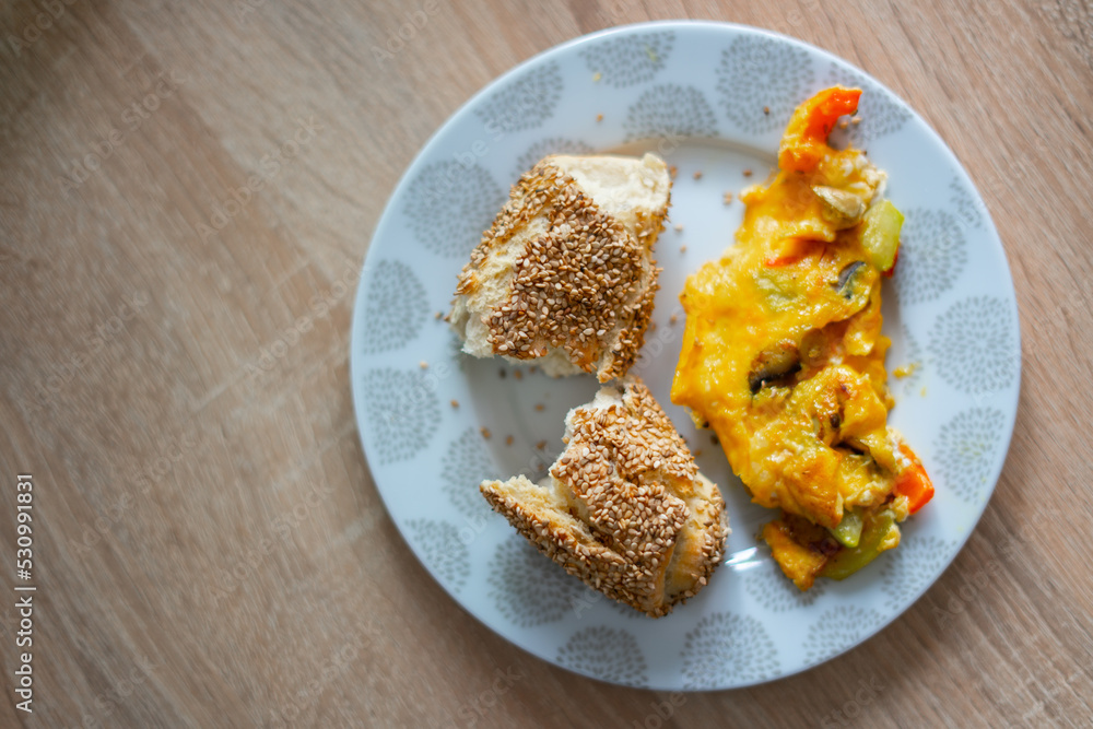 Bread with sesame seeds and scrambled eggs with peppers, tomatoes and mushrooms in a plate on a wooden table Bread with sesame seeds and scrambled eggs with peppers, tomatoes and mushrooms in a plate on a wooden table