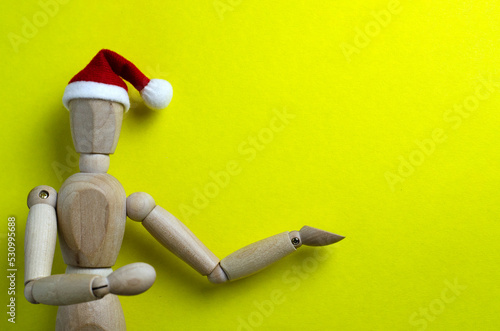 a man toy in a santa hat on a yellow background points to an empty background, a background image for a holiday 