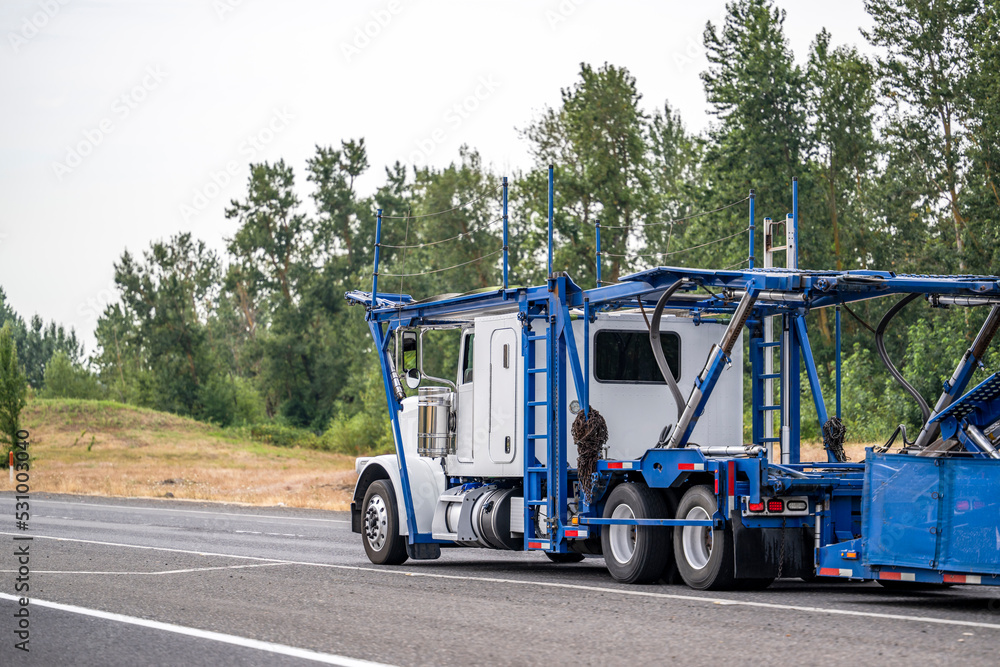 Car hauler big rig semi truck with empty modular semi trailer running on the highway entrance line