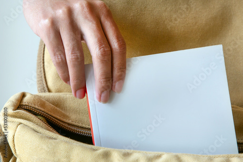 Obraz na plátně Hand putting white cover book into a bag