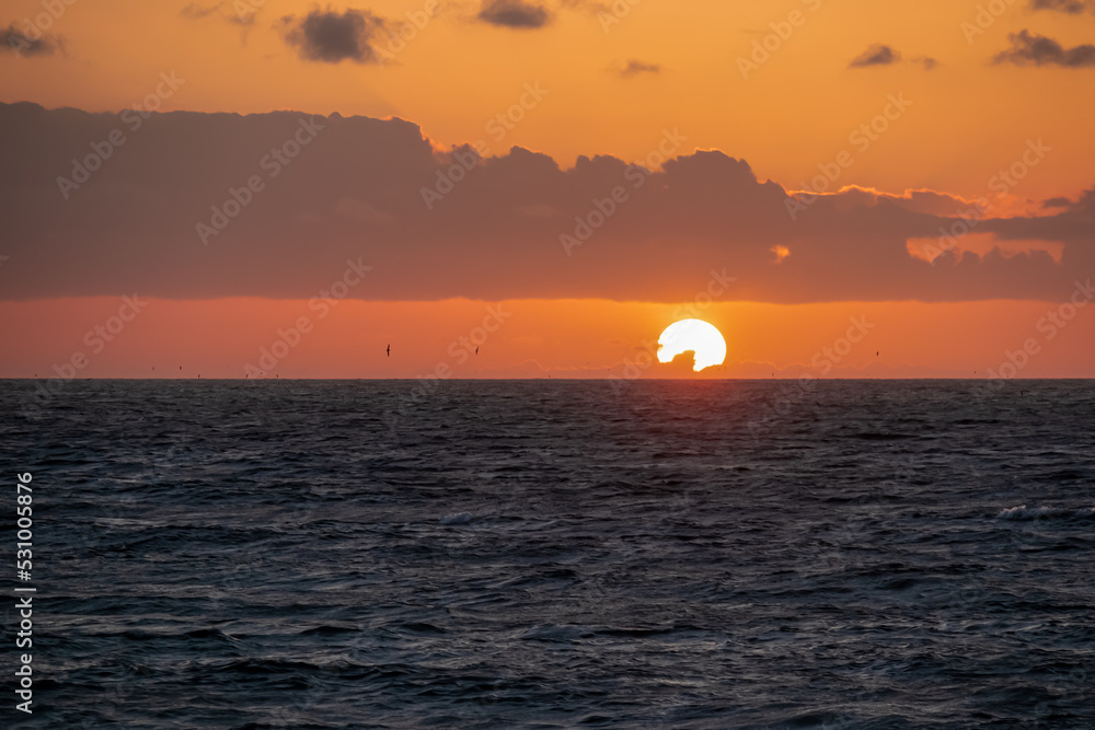 Scenic view during sunset from the beach Playa del Ingles in Valle Gran Rey, La Gomera, Canary Islands, Spain, Europe. Clouds emerging and turning orange red. Sun is going down behind the horizon