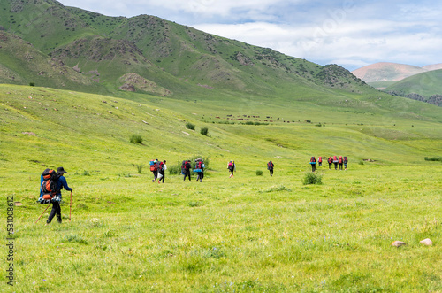 Back view of group of tourists walking with big backpacks in the mountain valey.