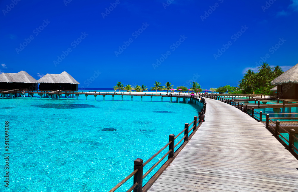 Landscape on Maldives island, luxury water villas resort and wooden pier. Beautiful sky and ocean and beach with palms background for summer vacation holiday and travel concept. Luxury travel.
