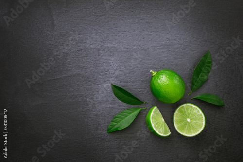 Green lime with sliced and green leaf on black dark background , top view , flat lay.