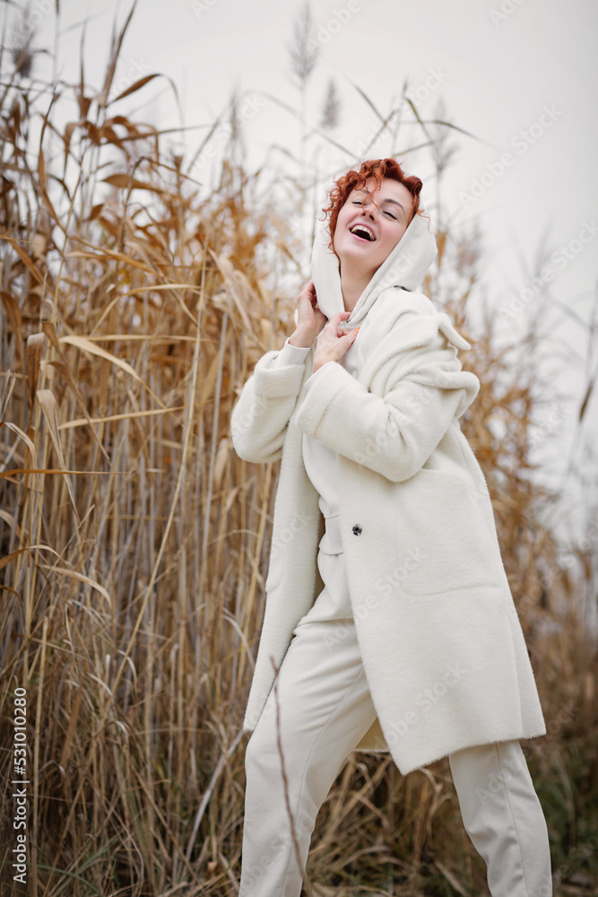 Pretty young woman in trendy white clothes poses in motion against the backdrop of an autumn landscape with dry reeds Pretty young woman in trendy white clothes poses in motion against the backdrop of an autumn landscape with dry reeds