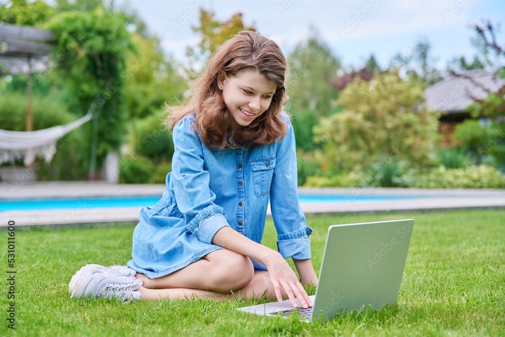 Preteen girl sitting on backyard lawn using laptop for leisure and study Preteen girl sitting on backyard lawn using laptop for leisure and study