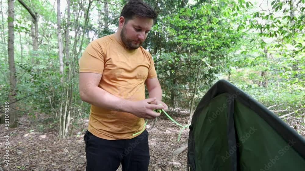 Angry man fails to untie a knot of a tent rope at a forest campsite ...