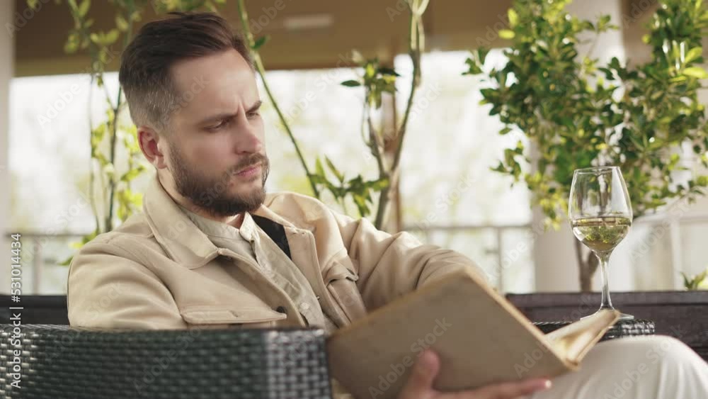 One Man Sitting at Restaurant on Weekend and Reading Book with Glass of Natural White Wine. Alone Person at Bar Drinking Tasty Alcohol Beverage of Clean Wineglass Cup. Abstract Background with Plants One Man Sitting at Restaurant on Weekend and Reading Book with Glass of Natural White Wine. Alone Person at Bar Drinking Tasty Alcohol Beverage of Clean Wineglass Cup. Abstract Background with Plants