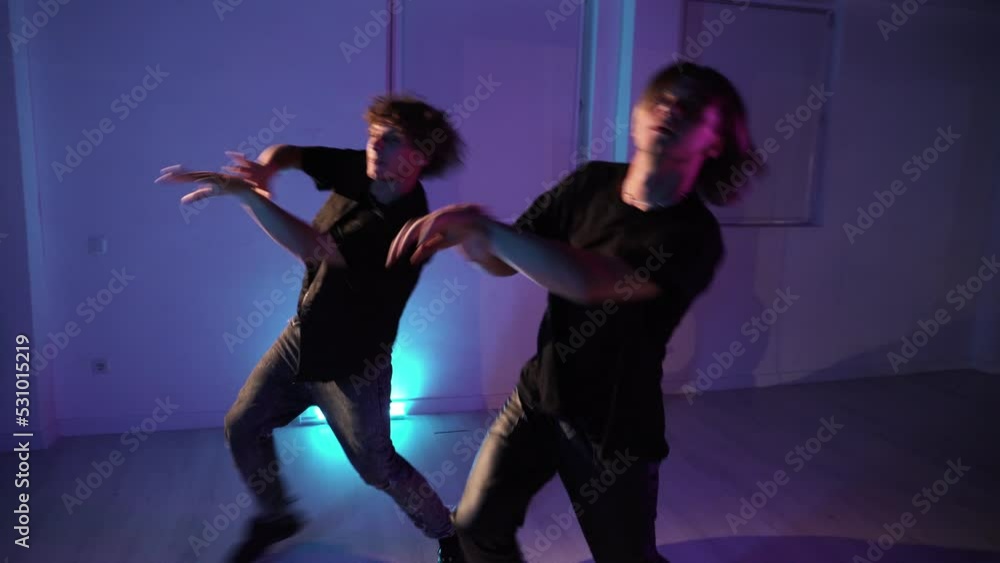 Two professional twin dancers dancing modern dance in the dance hall in neon light Two professional twin dancers dancing modern dance in the dance hall in neon light