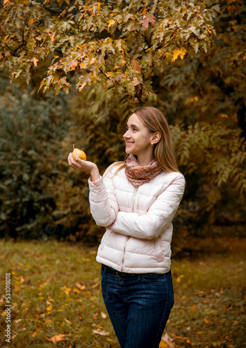beautiful smiling girl in pink sort jacket holding yellow pear in her hands in autumn park