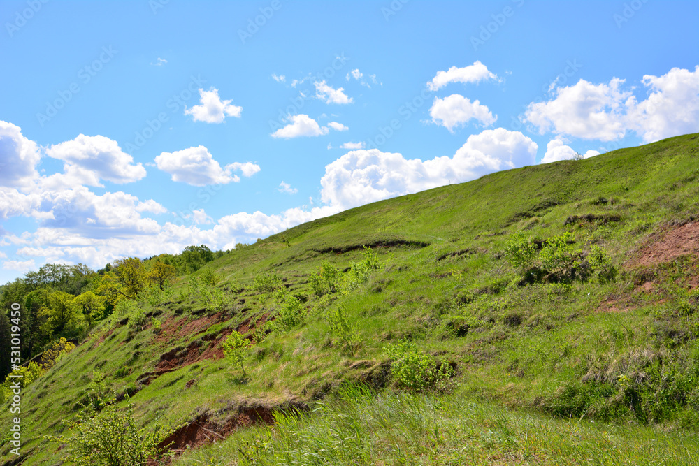 Naklejka premium green hill with blue sky and white clouds on background