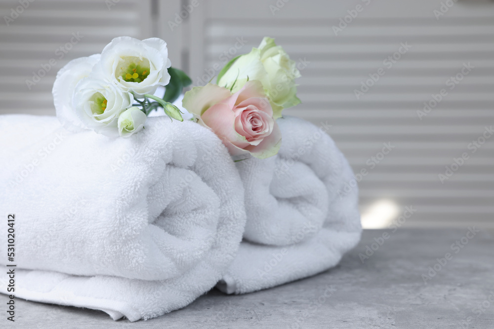 Rolled towels and flowers on grey table indoors Rolled towels and flowers on grey table indoors