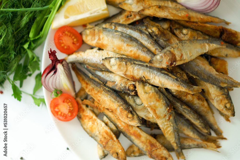 Fried small herring is laid out on a white plate. Fried small herring is laid out on a white plate.