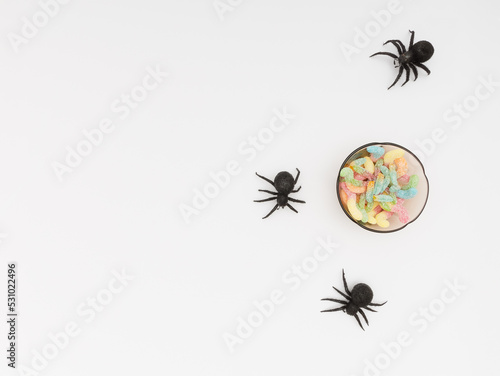 Some black toy spiders and a bowl full of candy. White background
