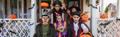 girls showing scary gestures near multiethnic friends in halloween costumes, banner