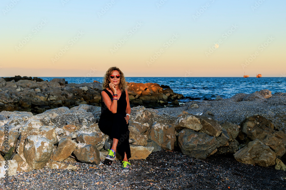 Woman sitting on rocks on beach at sunset