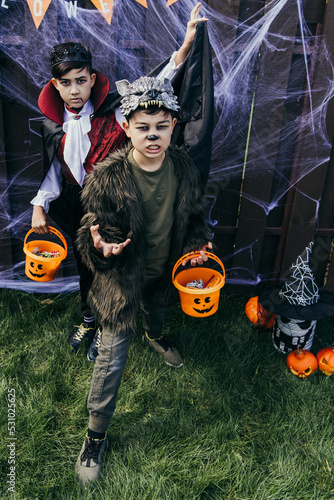 Asian boys in halloween costumes holding buckets with candies in backyard