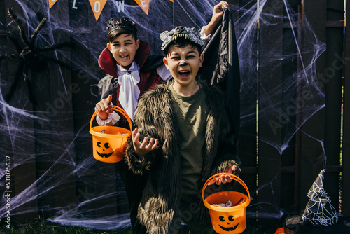 Asian kids in costumes holding halloween buckets and grimacing near fence outdoors