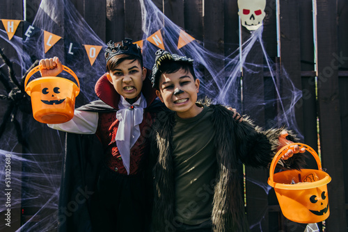 Asian kids with makeup grimacing at camera while holding buckets during halloween party outdoors