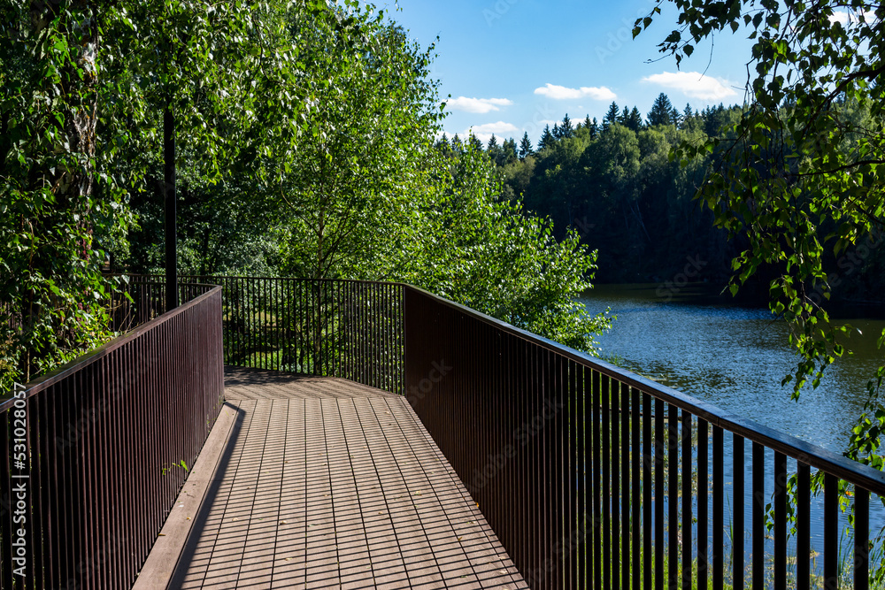 A beautiful promenade overlooking the lake, wooden walkways with railings. Pond on Stradalovka in Balabanovo, Russia