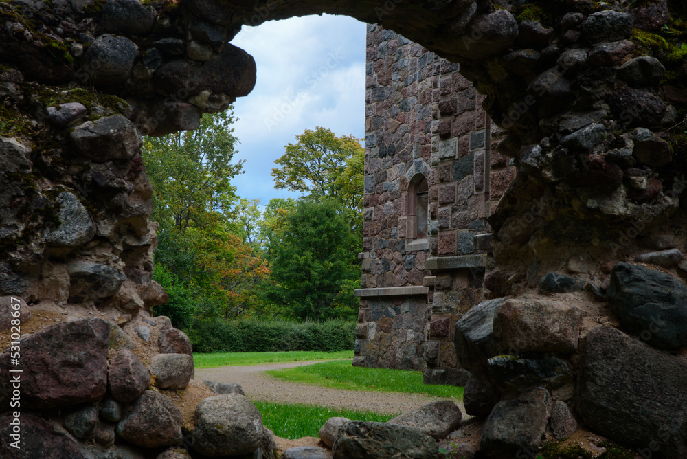 a beautiful castle wall with a crumbling hole where a path and trees can be seen in the distance on a cloudy day in autumn